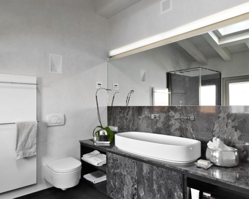 Interior of a modern bathroom in the attic with wooden beam ceiling and in the foreground on the right side the sink cabinet with a countertop sink above it the large mirror in the background the toilet near the radiator