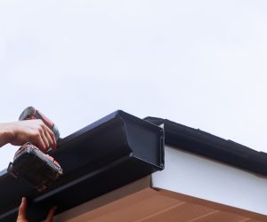 Worker installing rain gutter on roof is mounting downpipe